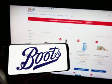 Stuttgart, Germany - 07-01-2023: Person holding mobile phone with logo of British pharmacy company Boots UK Limited on screen in front of web page. Focus on phone display. clipart