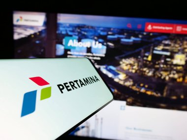 Stuttgart, Germany - 06-30-2023: Mobile phone with logo of Indonesian company PT Pertamina (Persero) on screen in front of website. Focus on center-right of phone display. clipart