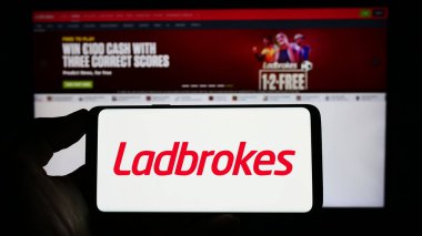 Stuttgart, Almanya - 06-30-2023: İnternet sayfası önünde üzerinde LC International Limited (Ladbrokes) şirketinin logosu bulunan cep telefonu sahibi kişi. Telefon ekranına odaklan.