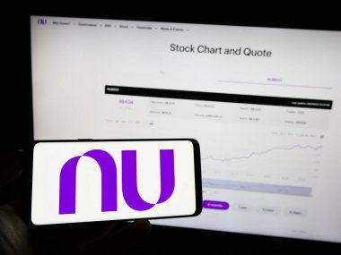 Stuttgart, Germany - 06-30-2023: Person holding mobile phone with logo of Brazilian company Nu Pagamentos S.A. (Nubank) on screen in front of web page. Focus on phone display. clipart