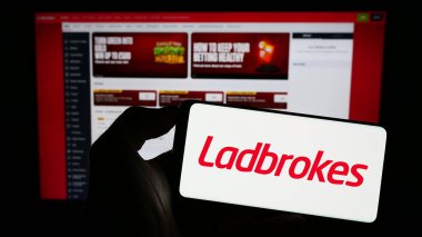 Stuttgart, Almanya - 06-30-2023: İnternet sayfası önünde LC International Limited (Ladbrokes) şirketinin logosuna sahip cep telefonu sahibi kişi. Telefon ekranına odaklan.