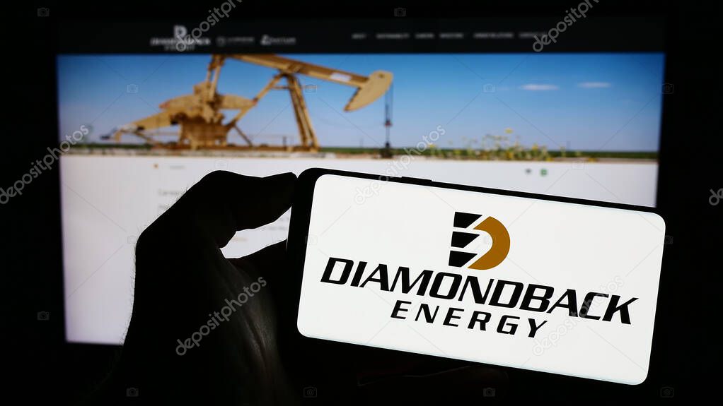 Stuttgart, Germany - 06-30-2023: Person holding cellphone with logo of American oil and gas company Diamondback Energy Inc. on screen in front of webpage. Focus on phone display.