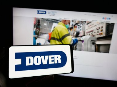 Stuttgart, Almanya - 06-28-2023: ABD 'li endüstriyel şirket Dover Corporation' ın logosuyla cep telefonu sahibi kişi iş sayfasının önünde ekranda görülüyor. Telefon ekranına odaklan.