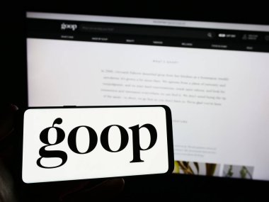 Stuttgart, Germany - 06-28-2023: Person holding smartphone with logo of US publishing and e-commerce company Goop Inc. on screen in front of website. Focus on phone display. clipart