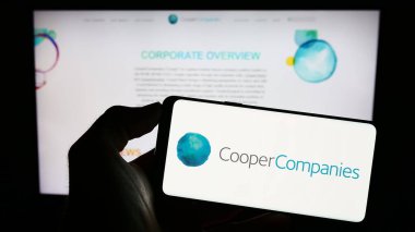 Stuttgart, Almanya - 06-25-2023: ABD 'li şirket The Cooper Companies Inc.' in logosuyla cep telefonu sahibi kişi iş sayfasının önünde ekranda. Telefon ekranına odaklan.