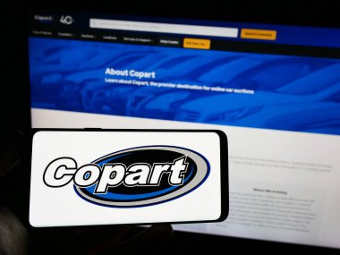 Stuttgart, Almanya - 06-25-2023: Amerikan otomotiv şirketi Copart Inc. 'in logosuna sahip cep telefonu sahibi kişi iş sayfasının önünde ekranda. Telefon ekranına odaklan.