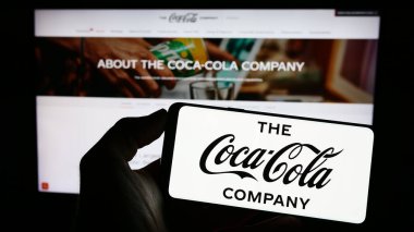 Stuttgart, Almanya: 06-25-2023: ABD 'li içecek işi logosu olan cep telefonu sahibi kişi The Coca-Cola Company web sayfasının önünde ekranda. Telefon ekranına odaklan.