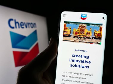 Stuttgart, Germany : 06-25-2023: Person holding cellphone with webpage of US energy company Chevron Corporation on screen in front of logo. Focus on center of phone display. clipart