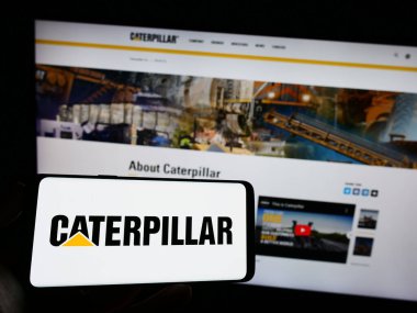 Stuttgart, Almanya - 06-25-2023: ABD 'li ağır ekipman şirketi Caterpillar Inc.' in logosuyla cep telefonu sahibi kişi iş sayfasının önünde ekranda. Telefon ekranına odaklan.