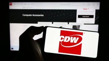 Stuttgart, Germany - 06-25-2023: Person holding smartphone with logo of US technology company CDW Corporation on screen in front of website. Focus on phone display. clipart