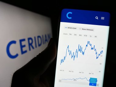 Stuttgart, Almanya - 06-25-2023: ABD 'li yazılım şirketi Ceridian HCM Holding Inc.' nin web sitesi ile cep telefonu tutan kişi logo ile ekranda. Telefon ekranının merkezine odaklan.