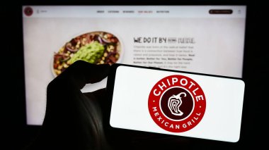 Stuttgart, Almanya - 06-25-2023: ABD 'li Chipotle Mexican Grill Inc. şirketinin logosunu elinde tutan kişi web sitesinin önünde ekranda. Telefon ekranına odaklan.