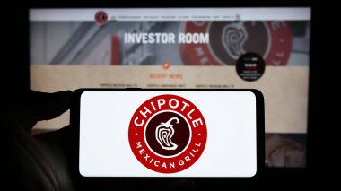 Stuttgart, Almanya - 06-25-2023: ABD 'li Chipotle Mexico Grill Inc. şirketinin logosunun bulunduğu cep telefonu sahibi kişi iş sayfasının önünde ekranda. Telefon ekranına odaklan.