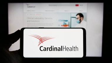 Stuttgart, Almanya - 06-25-2023: Web sitesi önünde ekranda ABD 'li sağlık şirketi Cardinal Health Inc.' in logosunun bulunduğu akıllı telefonu tutan kişi. Telefon ekranına odaklan.