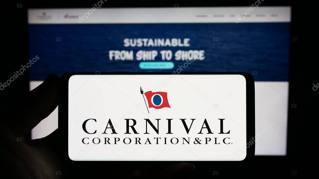 Stuttgart, Germany - 06-25-2023: Person holding smartphone with logo of cruise company Carnival Corporation plc on screen in front of website. Focus on phone display.