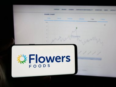 Stuttgart, Almanya - 11-13-2024: ABD 'li fırın gıda şirketi Flowers Foods Corporation' ın logosunu elinde tutan kişi web sitesinin önünde ekranda. Telefon ekranına odaklan.