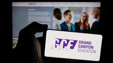 Stuttgart, Germany - 11-14-2024: Person holding mobile phone with logo of US company Grand Canyon Education Inc. (GCE) on screen in front of web page. Focus on phone display. clipart