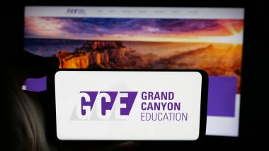 Stuttgart, Germany - 11-14-2024: Person holding cellphone with logo of US company Grand Canyon Education Inc. (GCE) on screen in front of business webpage. Focus on phone display. clipart