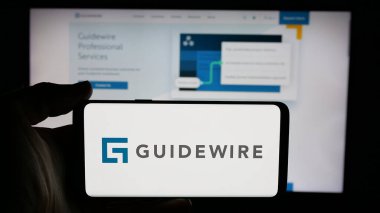 Stuttgart, Germany - 11-14-2024: Person holding cellphone with logo of US company Guidewire Software Inc. on screen in front of business webpage. Focus on phone display. clipart