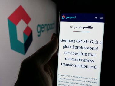 Stuttgart, Almanya - 11-14-2024: ABD 'li bilgi teknolojisi şirketi Genpact Ltd.' nin internet sayfası ile cep telefonu elinde bulunan kişi logolu ekranda. Telefon ekranının merkezine odaklan.