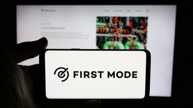 Stuttgart, Almanya - 11-17-2024: Batarya şirketi First Mode Holding Inc. 'nin logosuyla cep telefonu sahibi kişi iş sayfasının önünde ekranda. Telefon ekranına odaklan.
