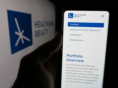 Stuttgart, Almanya - 11-26-2024: ABD 'li emlak şirketi Healthcare Realty Trust Inc.' in web sayfası ile cep telefonu sahibi kişi logo ile ekranda. Telefon ekranının merkezine odaklan.
