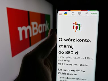 Stuttgart, Almanya - 11-26-2024: Polonyalı bankacılık şirketi mBank S.A. 'nın web sayfası ile cep telefonu sahibi kişi iş logosu önünde ekranda. Telefon ekranının merkezine odaklan.