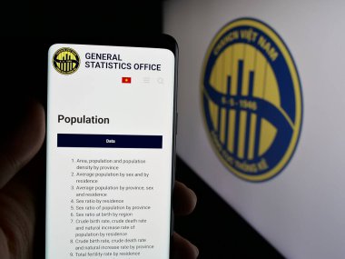 Stuttgart, Germany - 11-25-2024: Person holding smartphone with webpage of General Statistics Office of Vietnam (GSO) on screen with logo. Focus on center of phone display. clipart