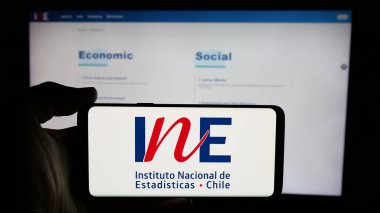 Stuttgart, Almanya - 11-25-2024: İnternet sayfası önünde üzerinde Instituto Nacional de Estadistica de Chile (INE) logosu bulunan kişi. Telefon ekranına odaklan.