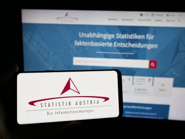 Stuttgart, Almanya - 11-25-2024: İnternet sitesi önünde üzerinde federal istatistik bürosu Statistik Avusturya 'nın logosu bulunan akıllı telefon sahibi kişi. Telefon ekranına odaklan.