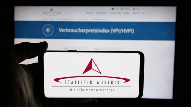 Stuttgart, Almanya - 11-25-2024: İnternet sayfası önündeki ekranda federal istatistik bürosu Statistik Avusturya 'nın logosuna sahip cep telefonu sahibi kişi. Telefon ekranına odaklan.