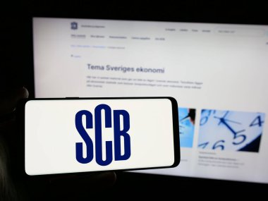 Stuttgart, Almanya - 11-24-2024: İnternet sitesi önünde üzerinde İstatistik Merkezi (İsveç İstatistik Bölümü, SCB) logosu olan akıllı telefon sahibi kişi. Telefon ekranına odaklan.