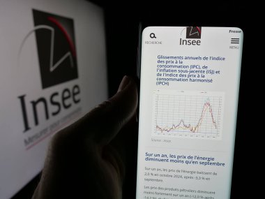 Stuttgart, Germany - 11-20-2024: Person holding cellphone with webpage of French national statistics agency INSEE on screen in front of logo. Focus on center of phone display. clipart