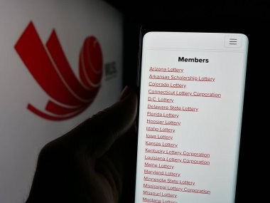 Stuttgart, Germany - 11-20-2024: Person holding smartphone with webpage of organisation Multi-State Lottery Association (MUSL) on screen with logo. Focus on center of phone display. clipart