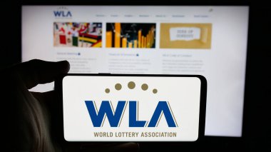 Stuttgart, Almanya - 11-20-2024: İnternet sayfası önünde Dünya Piyango Derneği (WLA) logosu olan cep telefonu sahibi kişi. Telefon ekranına odaklan.