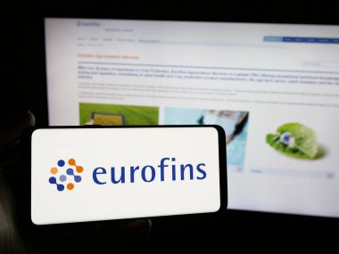 Stuttgart, Almanya - 11-18-2024: Laboratuvar şirketi Eurofins Scientific SE 'nin logosunu elinde tutan kişi web sitesinin önünde ekranda. Telefon ekranına odaklan.
