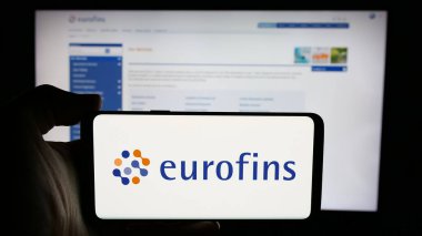 Stuttgart, Almanya - 11-18-2024: Laboratuvar şirketi Eurofins Scientific SE 'nin logosuyla cep telefonu sahibi kişi iş sayfası önünde ekranda. Telefon ekranına odaklan.
