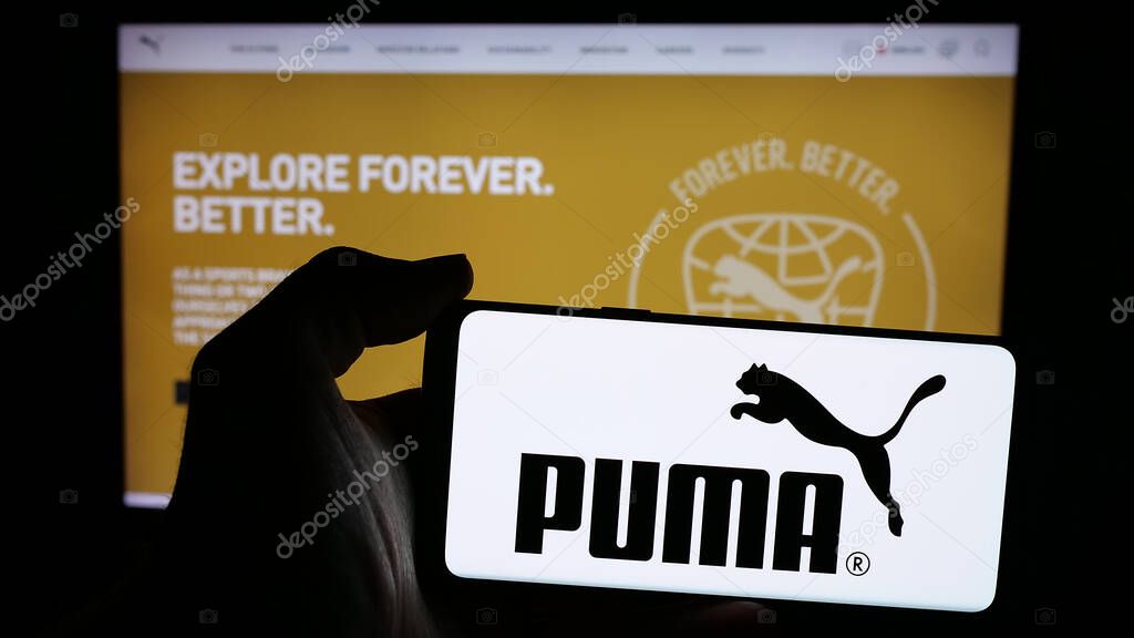 Stuttgart, Germany - 11-20-2024: Person holding mobile phone with logo of German footwear and apparel company Puma SE on screen in front of web page. Focus on phone display.