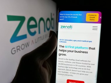 Stuttgart, Almanya - 11-15-2024: ABD 'li güzellik yazılım şirketi Soham Inc. (Zenoti)' nin web sitesi ile cep telefonu tutan kişi logolu ekranda. Telefon ekranının merkezine odaklan.