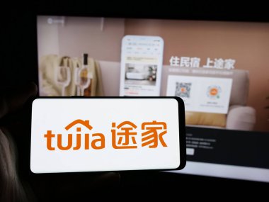 Stuttgart, Almanya - 11-15-2024: Çinli emlak platformu şirketi Tujia 'nın logosunu elinde tutan kişi web sitesinin önünde ekranda. Telefon ekranına odaklan.