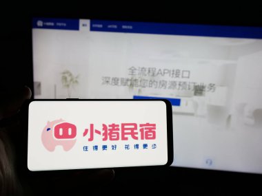 Stuttgart, Almanya - 11-15-2024: Çinli emlak platformu şirketi Xiaozhu 'nun logosunu elinde tutan kişi web sitesinin önünde ekranda. Telefon ekranına odaklan.