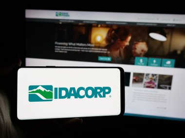 Stuttgart, Almanya - 11-26-2024: İnternet sitesi önünde üzerinde ABD 'li elektrik şirketi IDACORP Inc.' in logosu bulunan akıllı telefon sahibi kişi. Telefon ekranına odaklan.