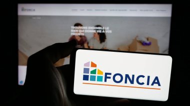 Stuttgart, Almanya - 11-26-2024: Fransız emlak şirketi Foncia SAS 'ın logosuyla cep telefonu sahibi kişi iş sayfasının önünde ekranda. Telefon ekranına odaklan.