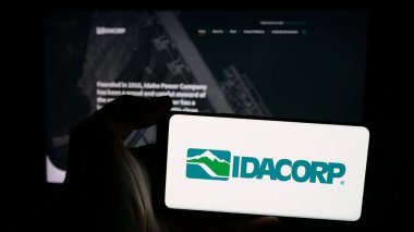 Stuttgart, Almanya - 11-26-2024: Amerikan elektrik şirketi IDACORP Inc. 'in logosuna sahip cep telefonu sahibi kişi iş sayfasının önünde ekranda. Telefon ekranına odaklan.
