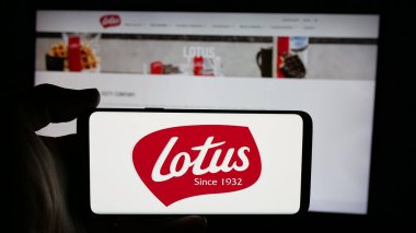Stuttgart, Almanya - 11-27-2024: Belçikalı abur cubur şirketi Lotus Fırın NV 'nin logosuyla cep telefonu sahibi kişi web sitesinin önünde ekranda. Telefon ekranına odaklan.