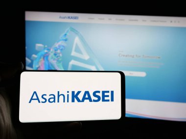 Stuttgart, Almanya - 11-27-2024: Japon kimya şirketi Asahi Kasei Corporation 'ın logosunu elinde tutan kişi web sitesinin önünde ekranda. Telefon ekranına odaklan.
