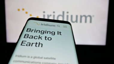 Stuttgart, Germany - 11-28-2024: Smartphone with website of US satellite company Iridium Communications Inc. on screen in front of business logo. Focus on top-elft of phone display. clipart