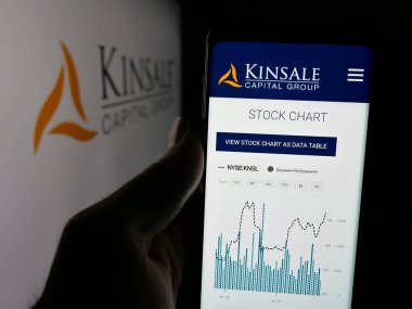 Stuttgart, Germany - 11-28-2024: Person holding cellphone with webpage of US insurance company Kinsale Capital Group Inc. on screen with logo. Focus on center of phone display. clipart