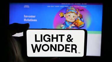 Stuttgart, Almanya - 11-28-2024: ABD 'li kumar şirketi Light and Wonder Inc.' in logosuyla cep telefonu sahibi kişi iş sayfasının önünde ekranda. Telefon ekranına odaklan.