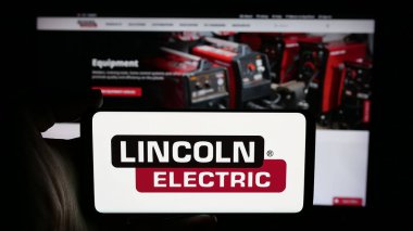 Stuttgart, Almanya - 11-28-2024: ABD 'li Lincoln Electric Holding Inc. şirketinin logosuyla cep telefonu sahibi kişi iş sayfası önünde ekranda. Telefon ekranına odaklan.